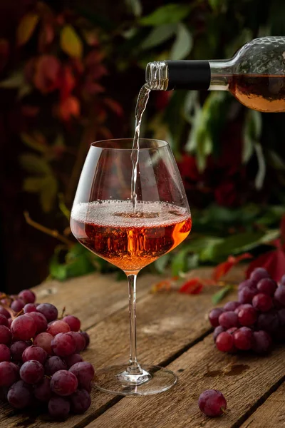 Autumn cozy romantic evening outdoors, wooden table with glass with rose wine, rose wine is poured from the bottle into the glass