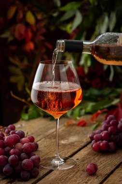 Sonbahar havası, açık havada romantik bir akşam, cam kaplı ahşap masa, gül şarabı şişeden bardağa dökülüyor.