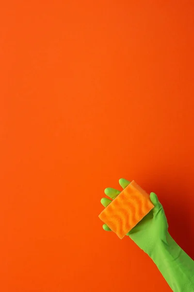 一只手戴着绿色橡胶防护手套 手拿着在橙色背景上的洗涤海绵 — 图库照片