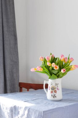 Masadaki sürahide pembe lale buketi, evin içinde çiçekler.