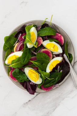 Salata, marul ve yumurta, kırmızı soğan ve Margelan turpu mermer bir arka planda yakın planda.