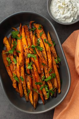 Portakallı fırın, oval seramik tabakta baharatlı tatlı patates kamışı ve yağ yoğurt ve baharatlı avokado sosu.