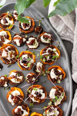 Fırında fırınlanmış portakallı tatlı patates yoğurt ve hurma, mikro yeşillikler serpiştirilmiş, gri oval seramik tabakta tatlı patates, üst manzara.