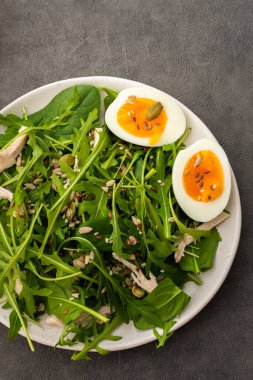 roka ve ıspanak ile nefis hafif salata, haşlanmış yumurta ve çeşitli sağlıklı tohumlar serpiştirilmiş tavuk göğsü gri arka planda, üst manzara
