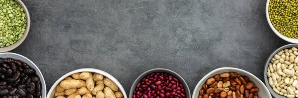 Banner of various types of legumes in bowls, green and yellow peas, chickpeas and peanuts, colored beans and lentils, mung beans and beans, top view, copy space