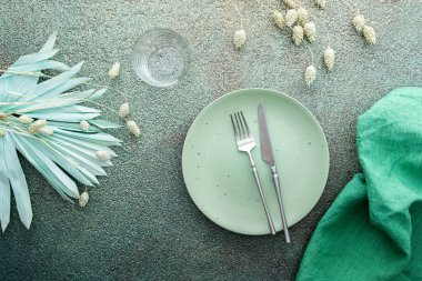 Masa ayarı, yeşil zemin üzerinde peçete ve çatal bıçak ile boş tabak, servis edilen masanın üst görünümü kuru çiçeklerle süslenmiş