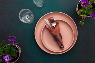 Masa ayarı, yeşil zemin üzerinde peçete ve çatal bıçak ile boş tabak servis edilen masanın üst görünümü hanım evladı çiçekleriyle süslenmiş.