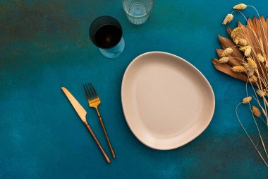 Masa ayarı, boş tabak ve turkuaz arka plan çatal bıçak takımı, kuru çiçeklerle süslenmiş servis edilen masanın üst görünümü