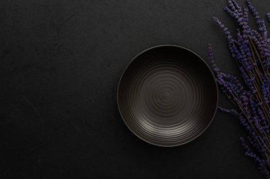 Masa ayarı, siyah zemin üzerinde çatal bıçak takımı olan boş tabak servis edilen masanın üst görüntüsü kuru lavanta çiçekleri