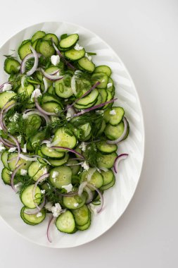 Beyaz oval tabakta salatalık, soğan ve peynir salatası.