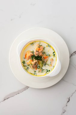 Norveç kırmızı somon balığı çorbası. Sebzeli, otlu ve kremalı. Beyaz mermer arka planda bir kase çorbanın üst görüntüsü.