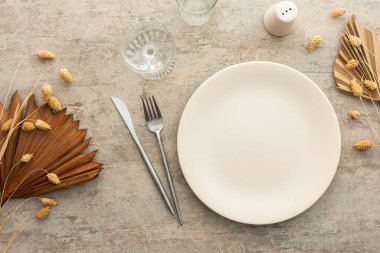 Kahverengi arkaplanda masa, tabak ve çatal bıçak seti, kuru çiçeklerle süslenmiş servis tablosunun üst görüntüsü