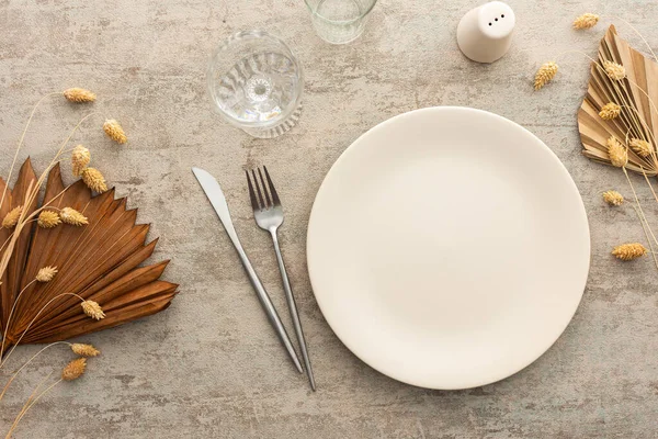 Kahverengi arkaplanda masa, tabak ve çatal bıçak seti, kuru çiçeklerle süslenmiş servis tablosunun üst görüntüsü