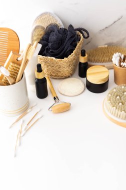 Seramik bardakta doğal tüyleri olan tahta diş fırçaları, yüz ve cilt bakım ürünleri, pipetli siyah şişeler ve bir kavanoz krem, banyo aksesuarları, spa ve güzellik konsepti.