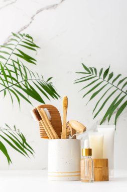 Seramik bardakta doğal tüyleri olan tahta diş fırçaları, yüz ve cilt bakım ürünleri, pipetli şişeler ve bir kavanoz krem, banyo aksesuarları, spa ve güzellik konsepti.