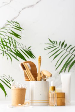 Seramik bardakta doğal tüyleri olan tahta diş fırçaları, yüz ve cilt bakım ürünleri, pipetli şişeler ve bir kavanoz krem, banyo aksesuarları, spa ve güzellik konsepti.