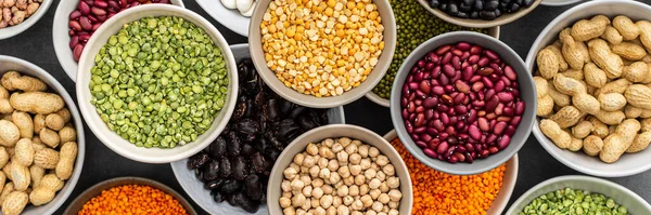 Banner of different types of legumes in bowls, green with yellow peas and mung beans, chickpeas and peanuts, colored beans and lentils, top view