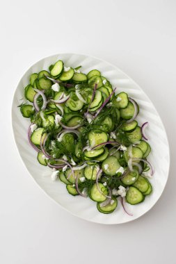 Beyaz oval tabakta salatalık, soğan ve peynir salatası.