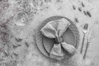 Masa ayarı, masada peçete ve çatal bıçak ile boş gri tabak, servis edilen masanın üst görüntüsü kuru çiçeklerle süslenmiş.