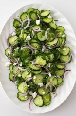 Beyaz oval tabakta salatalık, soğan ve peynir salatası.