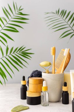 Seramik bardakta doğal tüyleri olan tahta diş fırçaları, yüz ve cilt bakım ürünleri, pipetli siyah şişeler ve bir kavanoz krem, banyo aksesuarları, spa ve güzellik konsepti.