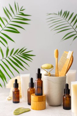 Seramik bardakta doğal tüyleri olan tahta diş fırçaları, yüz ve cilt bakım ürünleri, pipetli şişeler ve bir kavanoz krem, banyo aksesuarları, spa ve güzellik konsepti.