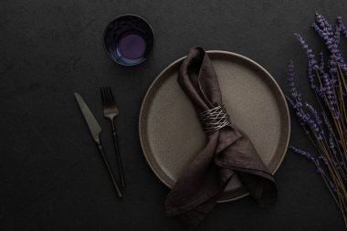 Masa ayarı, siyah zemin üzerinde peçete ve çatal bıçak takımı olan boş tabak servis edilen masa, kuru lavanta çiçekleri üst görünümü