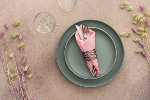 Masa ayarı, beton zeminde peçete ve çatal bıçaklı boş yeşil tabak, servis edilen masanın üst manzarası kuru çiçeklerle süslenmiş.
