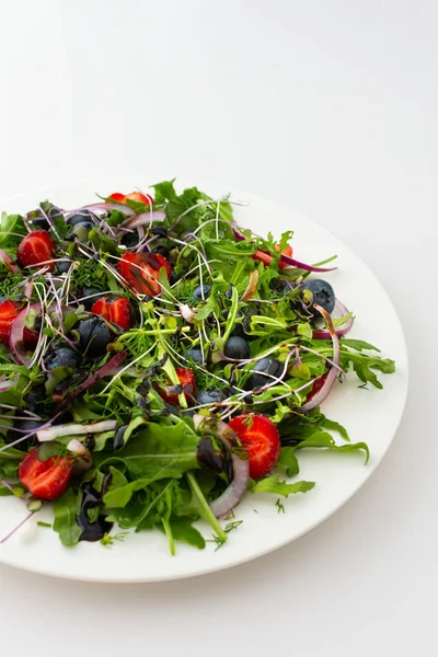 Light salad with arugula and berries, strawberries and blueberries, delicious healthy summer salad on a white background