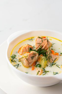 Norveç kırmızı somon balığı çorbası, sebze, ot ve krema, beyaz mermer arka planda bir kase çorba.