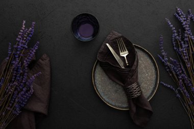 Masa ayarı, siyah zemin üzerinde peçete ve çatal bıçak takımı olan boş tabak servis edilen masa, kuru lavanta çiçekleri üst görünümü