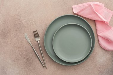 Masa ayarı, beton zeminde peçete ve çatal bıçaklı boş yeşil tabak, servis edilen masanın üst manzarası kuru çiçeklerle süslenmiş.