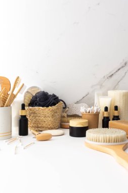 Seramik bardakta doğal tüyleri olan tahta diş fırçaları, yüz ve cilt bakım ürünleri, pipetli siyah şişeler ve bir kavanoz krem, banyo aksesuarları, spa ve güzellik konsepti.