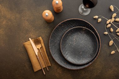 Masa ayarı, kahverengi bir zemin üzerinde peçete ve çatal bıçak ile boş gri tabak, servis edilen masanın üst görünümü kuru çiçeklerle süslenmiş