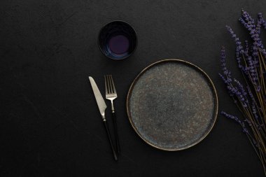 Masa ayarı, siyah zemin üzerinde çatal bıçak takımı olan boş tabak servis edilen masanın üst görüntüsü kuru lavanta çiçekleri