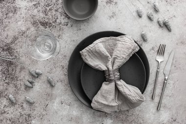 Masa ayarı, masada peçete ve çatal bıçak ile boş gri tabak, servis edilen masanın üst görüntüsü kuru çiçeklerle süslenmiş.