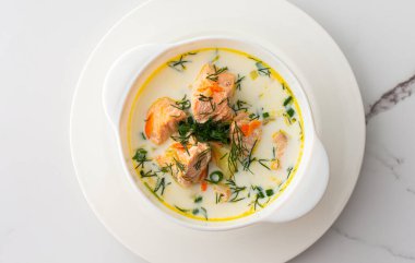 Norveç kırmızı somon balığı çorbası. Sebzeli, otlu ve kremalı. Beyaz mermer arka planda bir kase çorbanın üst görüntüsü.