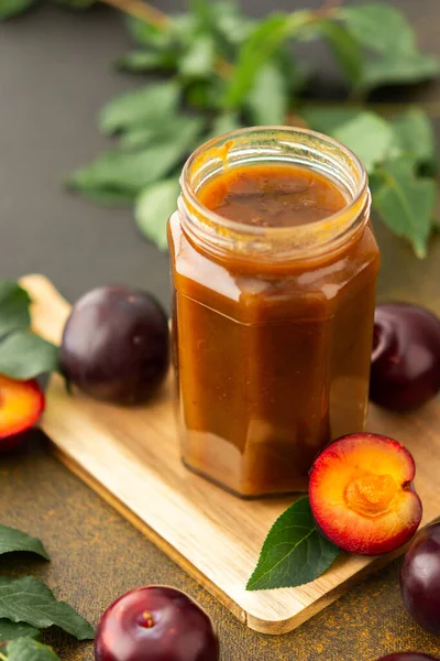 Homemade plum jam in a jar on a board with fresh plums, harvesting for the winter