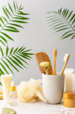 Seramik bardakta doğal tüyleri olan tahta diş fırçaları, yüz ve cilt bakım ürünleri, pipetli şişeler ve bir kavanoz krem, banyo aksesuarları, spa ve güzellik konsepti.