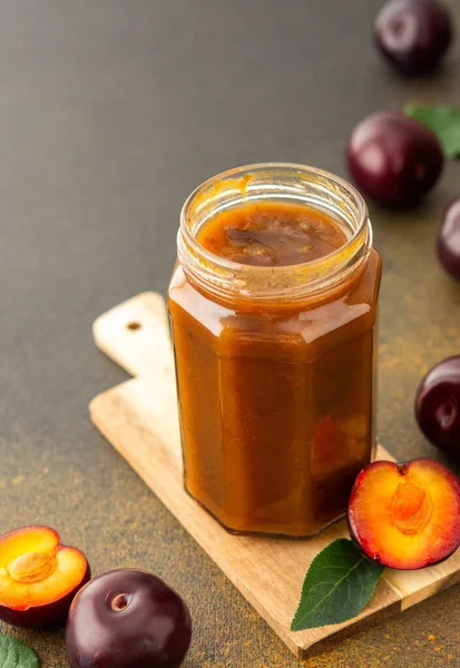 Homemade plum jam in a jar on a board with fresh plums, harvesting for the winter