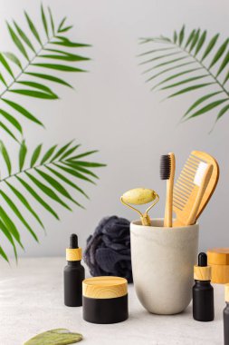 Seramik bardakta doğal tüyleri olan tahta diş fırçaları, yüz ve cilt bakım ürünleri, pipetli siyah şişeler ve bir kavanoz krem, banyo aksesuarları, spa ve güzellik konsepti.