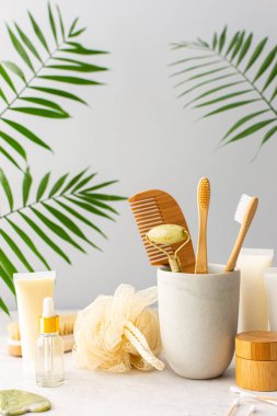 Seramik bardakta doğal tüyleri olan tahta diş fırçaları, yüz ve cilt bakım ürünleri, pipetli şişeler ve bir kavanoz krem, banyo aksesuarları, spa ve güzellik konsepti.