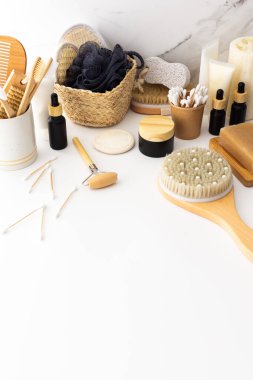 Seramik bardakta doğal tüyleri olan tahta diş fırçaları, yüz ve cilt bakım ürünleri, pipetli siyah şişeler ve bir kavanoz krem, banyo aksesuarları, spa ve güzellik konsepti.
