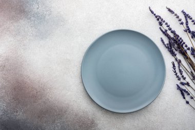 Masa ayarı, gri-pembe beton zemin üzerinde boş tabak, servis edilen masanın üst görüntüsü kuru lavanta çiçekleriyle süslenmiş.