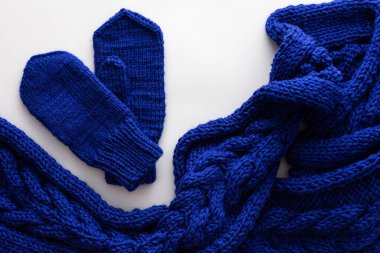 Beyaz arka planda mavi örülmüş yün atkı ve eldivenler, ev yapımı dikiş konsepti, üst görünüm.