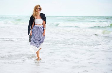 Gülümseyen olgun kadın deniz kıyısında yalınayak yürüyor. Denizde dinlenen bir kadın. Boşluğu kopyala.