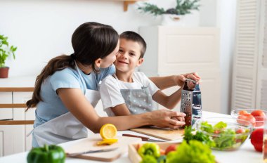 Bağlanma kavramı. Neşeli anne oğluna yemek pişirmede yardım ediyor, küçük çocuğa sağlıklı sebze salatası yapmayı öğretiyor, havuç rendeliyor, evde birlikte yemek pişiriyor..