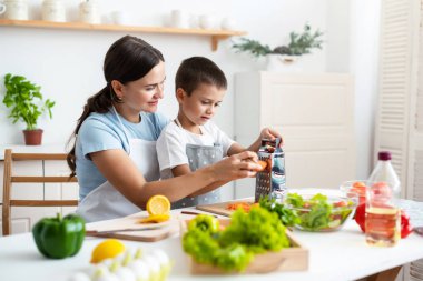 Bağlanma kavramı. Neşeli anne oğluna yemek pişirmede yardım ediyor, küçük çocuğa sağlıklı sebze salatası yapmayı öğretiyor, havuç rendeliyor, evde birlikte yemek pişiriyor..