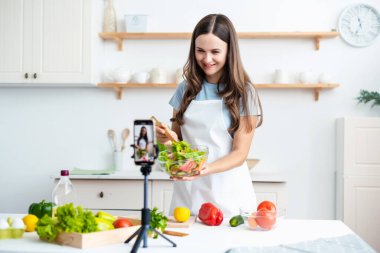 Genç kadın aşçı Webinar ana sınıfı dersi için internette yayınlanırken yemek pişiriyor. Kadın, ev mutfağında vejetaryen hazırlayan videolar yapıyor. Helthy gıda konsepti.