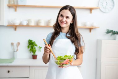 Beyaz önlük giyen gülümseyen aşçı kadın elinde sağlıklı taze salatayla kaseyi tutuyor. Yemek, aşçılık blogcuları konsepti.